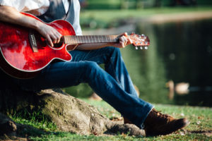 A guitarist playing their instrument near a pond.