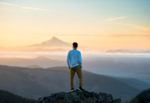 Man standing on top of a mountain observing the view and deep in thought about writing song lyrics.