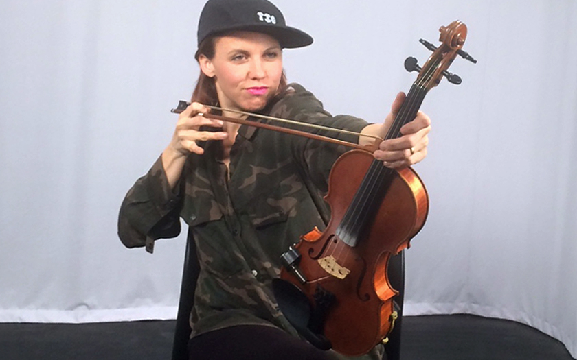 Alt text: Sarah Neufeld holds her 2007 Nathaniel Rowan violin aloft, as if she is using the bow as an arrow.