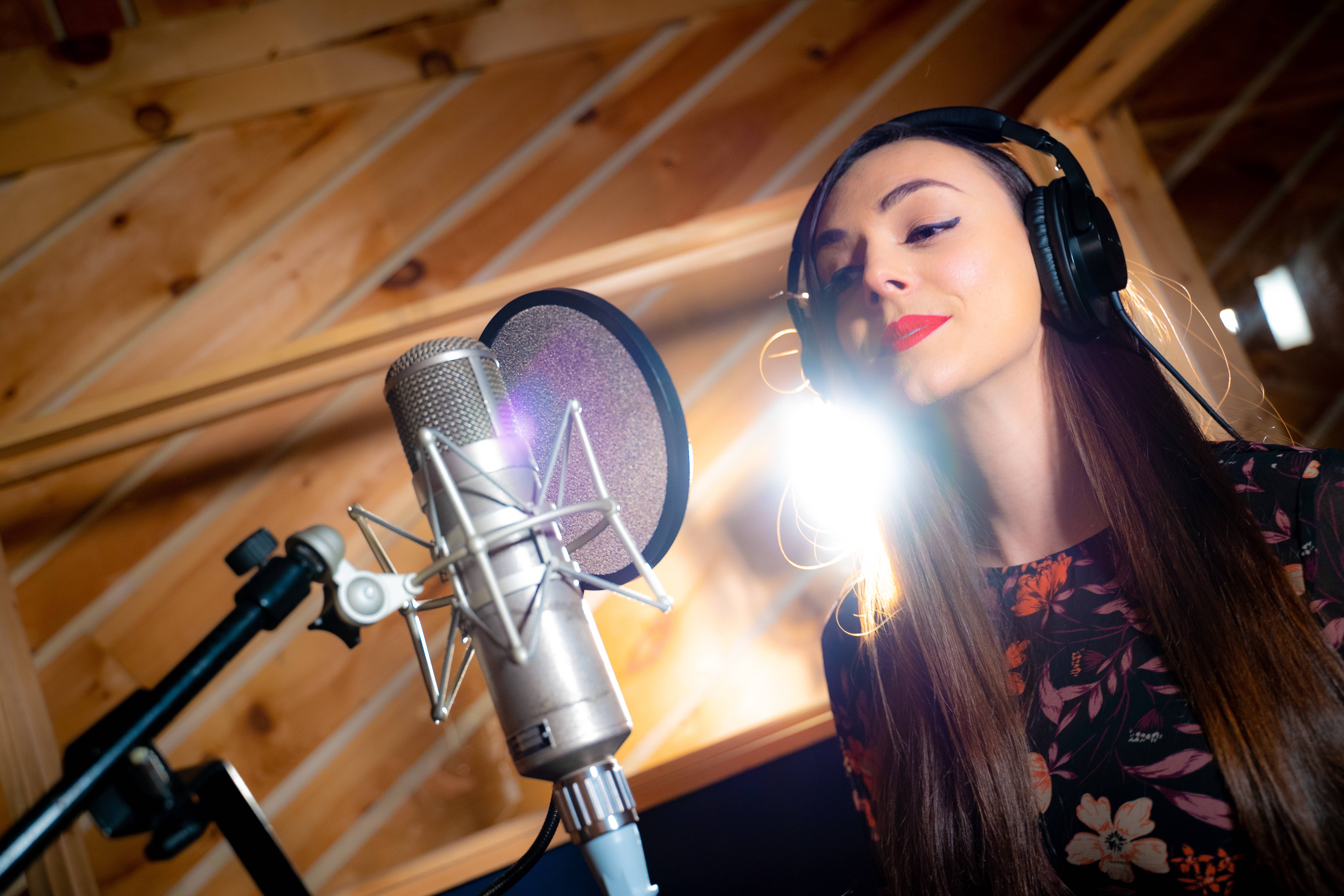 Berklee Online student Eirini Tornesaki singing into a microphone in a recording studio.