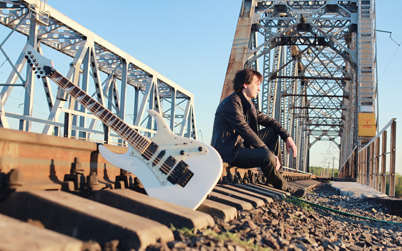 A musician with their guitar sitting on a bridge.