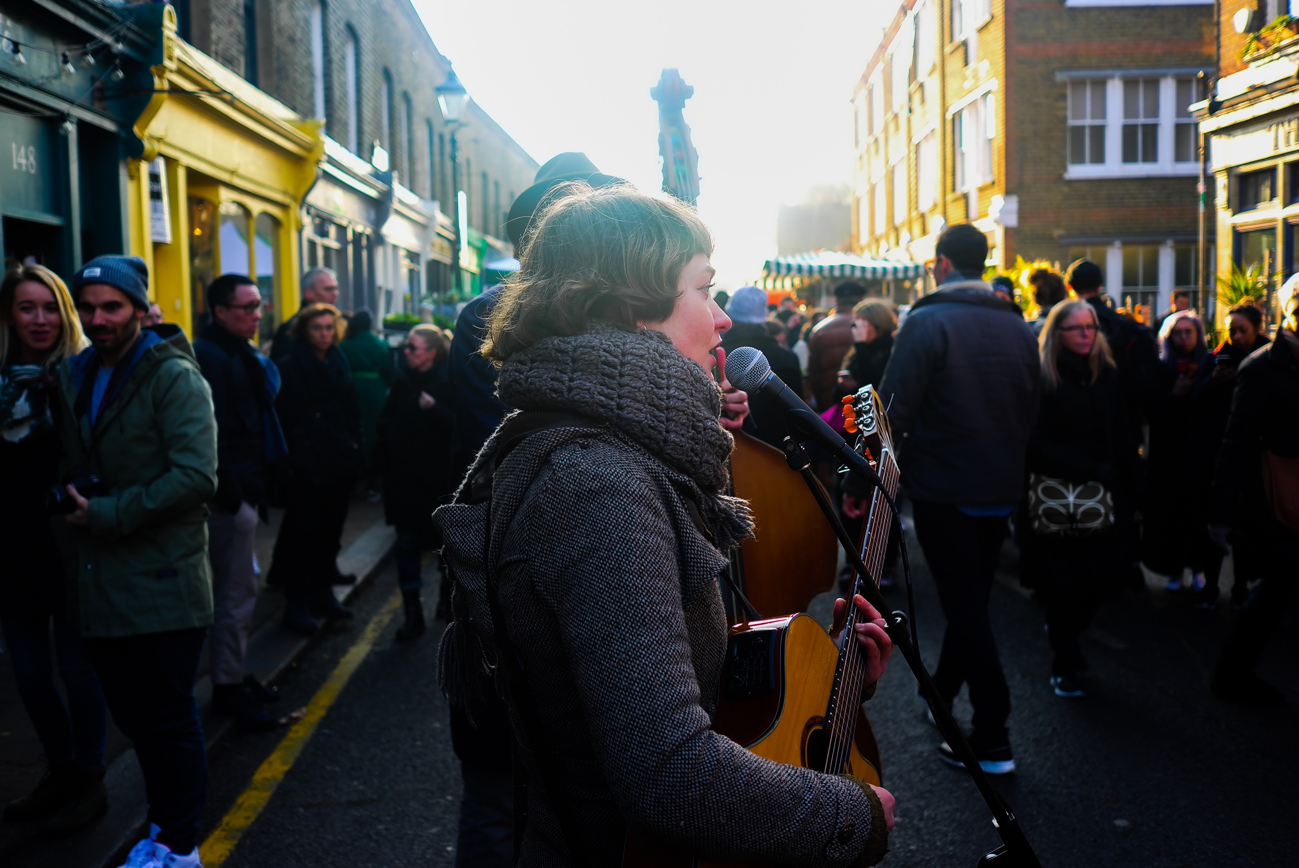 A woman stands outside in the cold, singing and performing music for a crowd of shoppers and revelers.