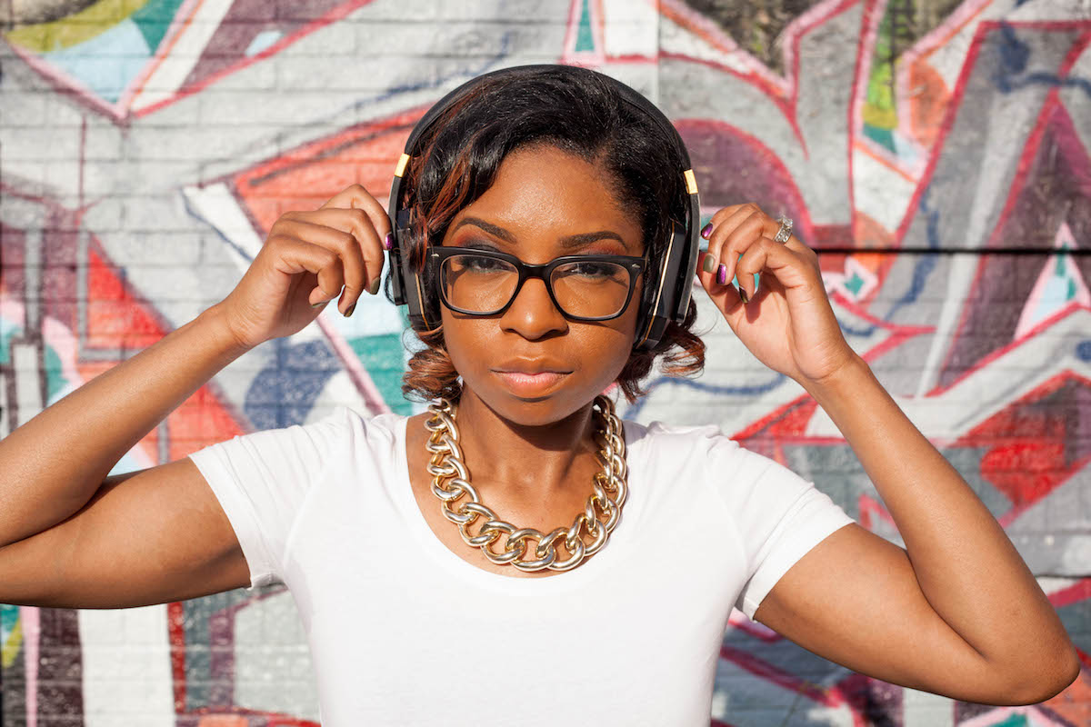 Gabrielle Davis stands in front of a colorful brick wall wearing headphones.