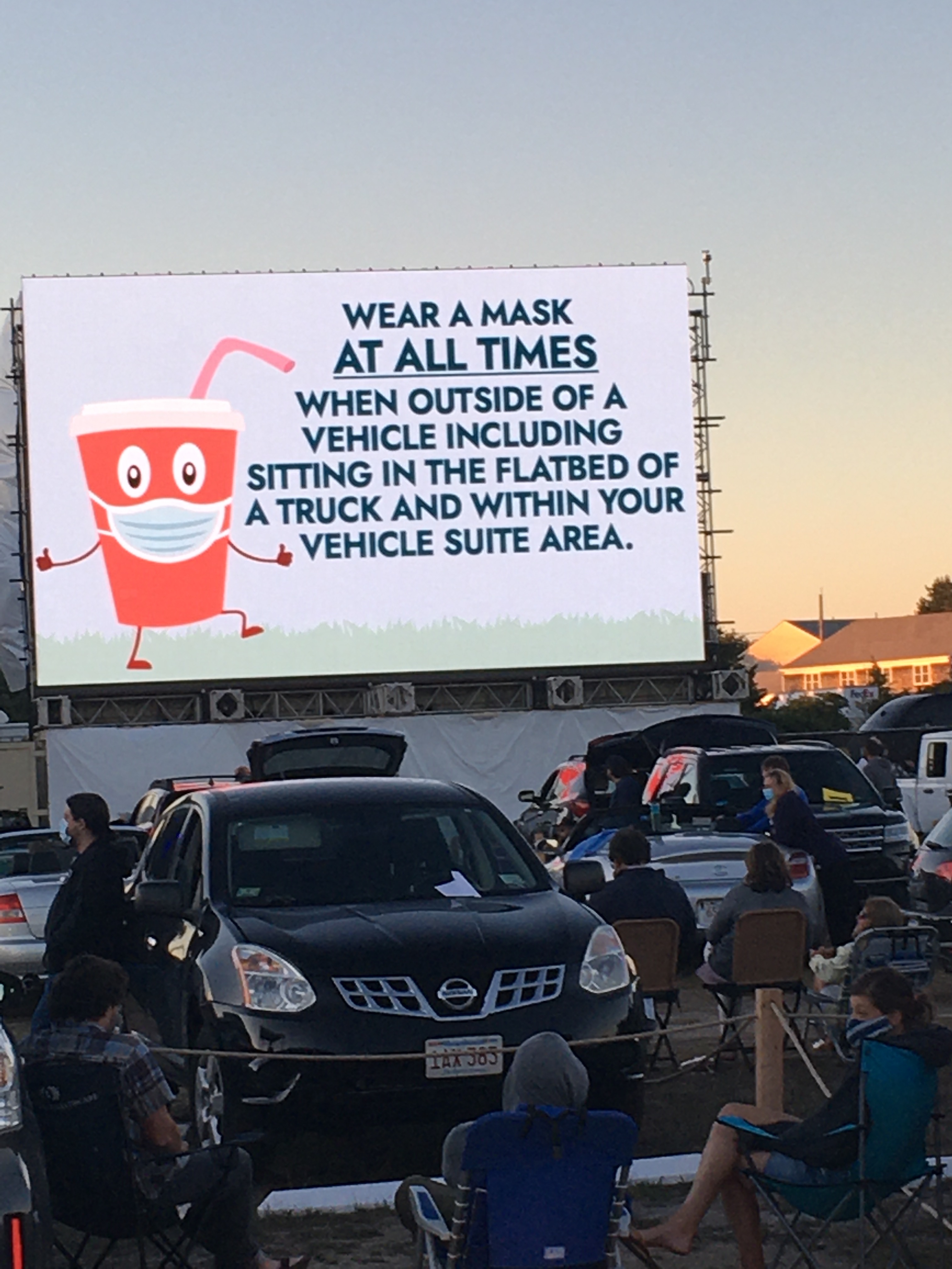 Signage during a drive-in concert at Yarmouth Drive-In shows a cup wearing a face mask and a foreboding message.