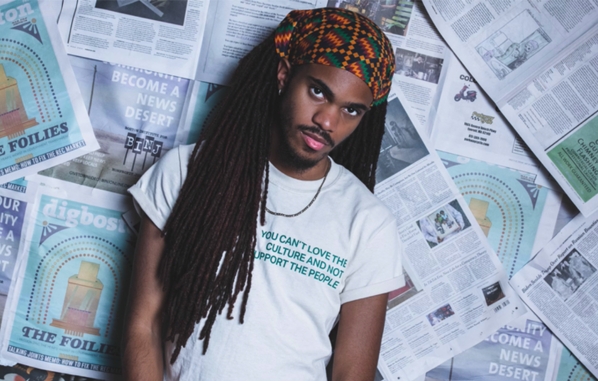 TikTok star Brandon Harris stands in front of a background of newspapers. His shirt reads: You can't love the culture and not support the people. 