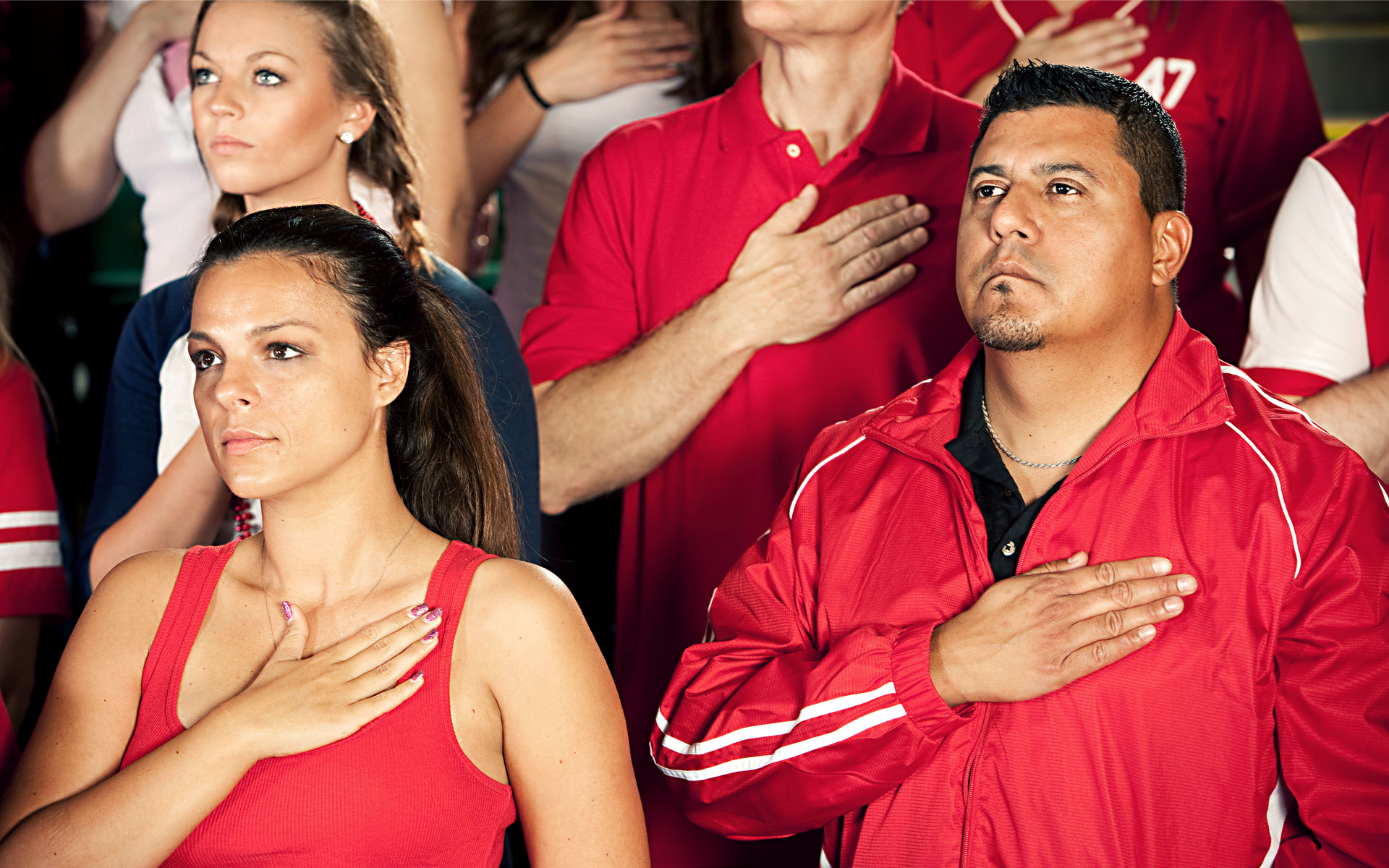 Attendees of a nondescript sporting event sing a nondescript national anthem for a nondescript country in this stock image.