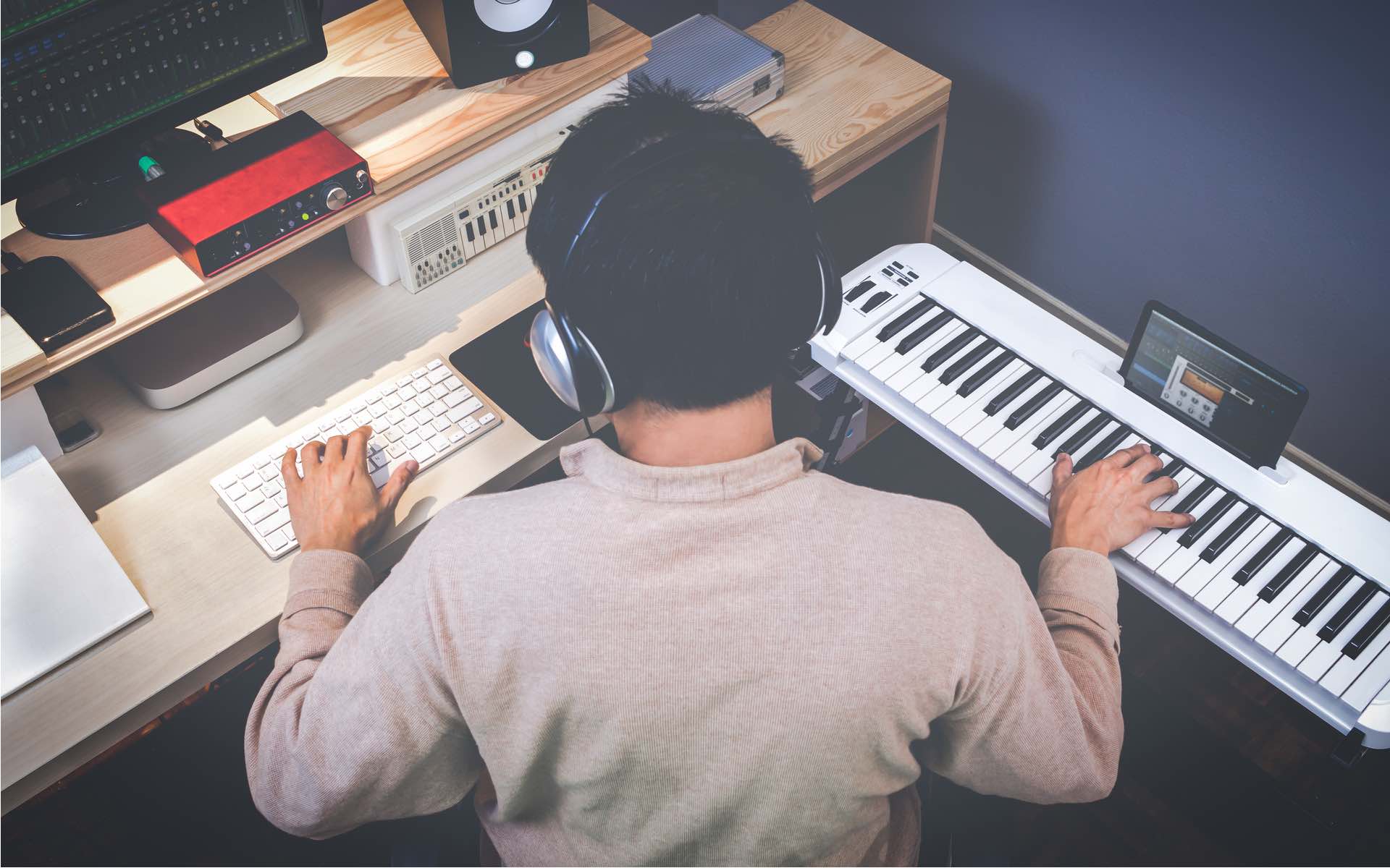 musician working at their computer and keyboard on a music composition