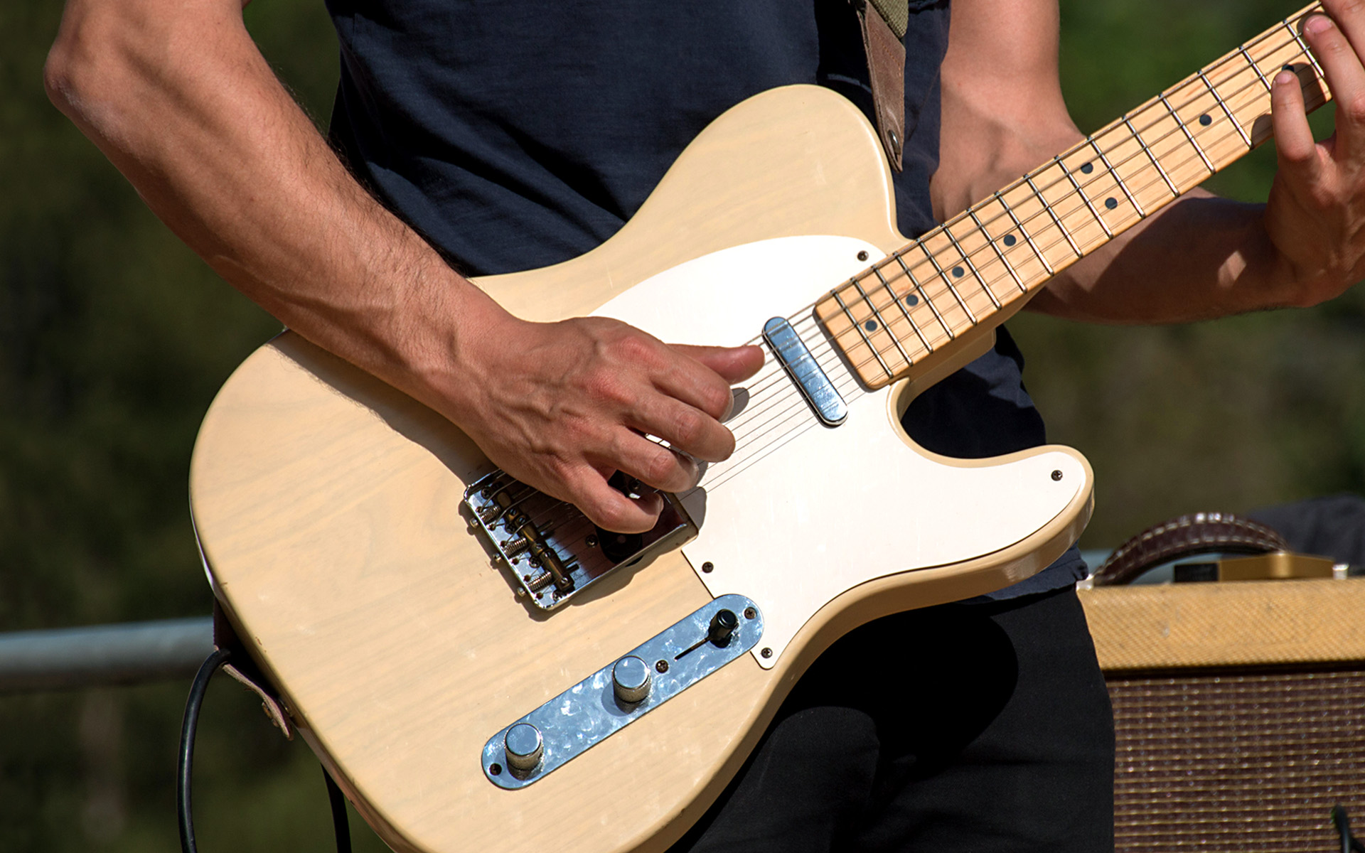 A muscular man plays a Fender Telecaster guitar, presumably delivering some hot country music licks.