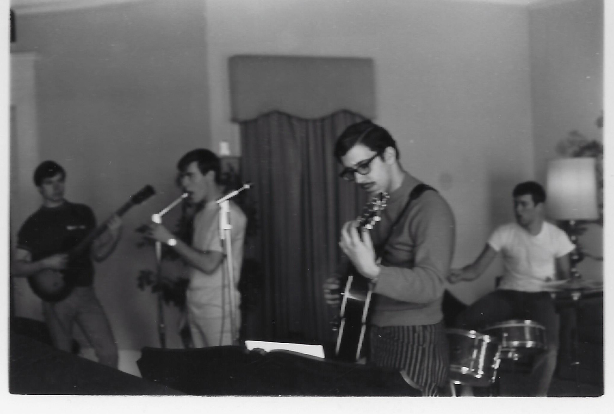A black and white photo of Richard Boyatzis rehearsing with three other bandmates in his MIT fraternity house in 1966. Boyatzis is playing guitar with other bandmates on bass, drums, and vocals.