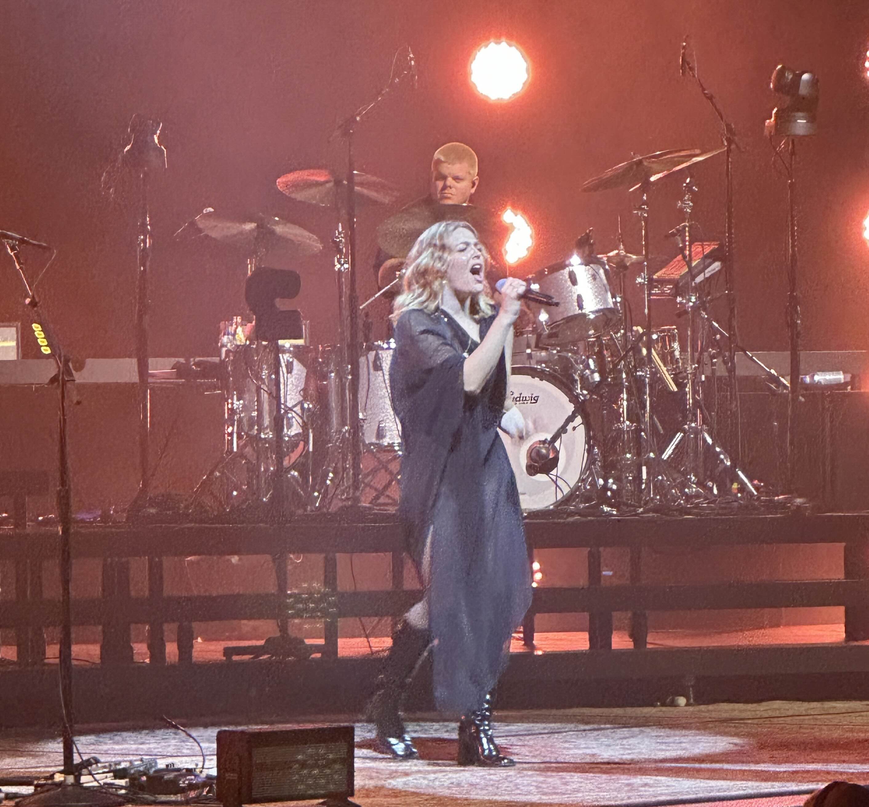 Jordan Rose playing drums behind Maggie Rogers while she's performing onstage at TD Garden in Boston.