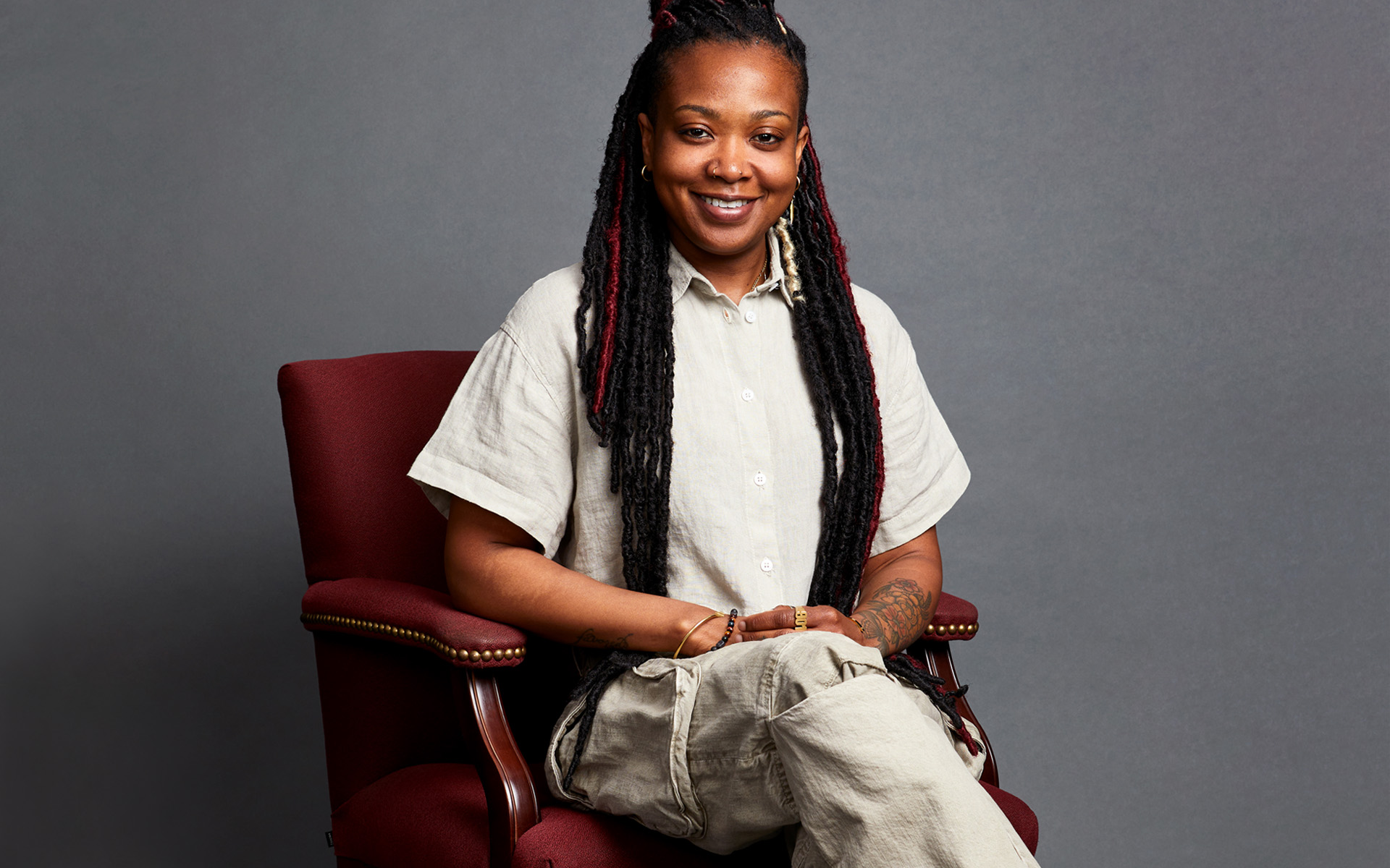 Amanda Davis, Berklee Online instructor and Sound Engineer for Janelle Monáe, is pictured sitting on a maroon chair, against a gray background.