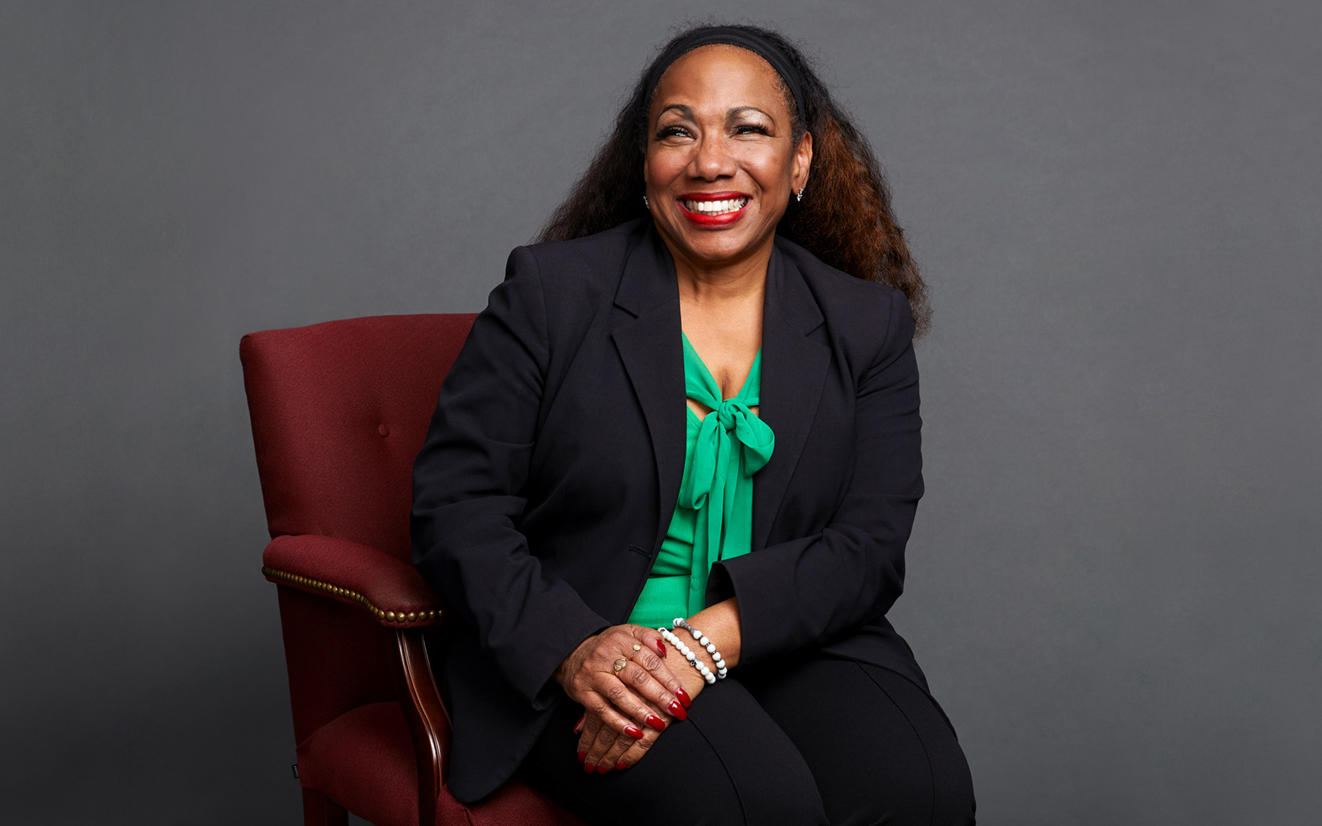 Gabrielle Goodman, Berklee Online instructor and singer, known for singing background with Chaka Khan and Roberta Flack, is pictured sitting on a maroon chair, against a gray background.