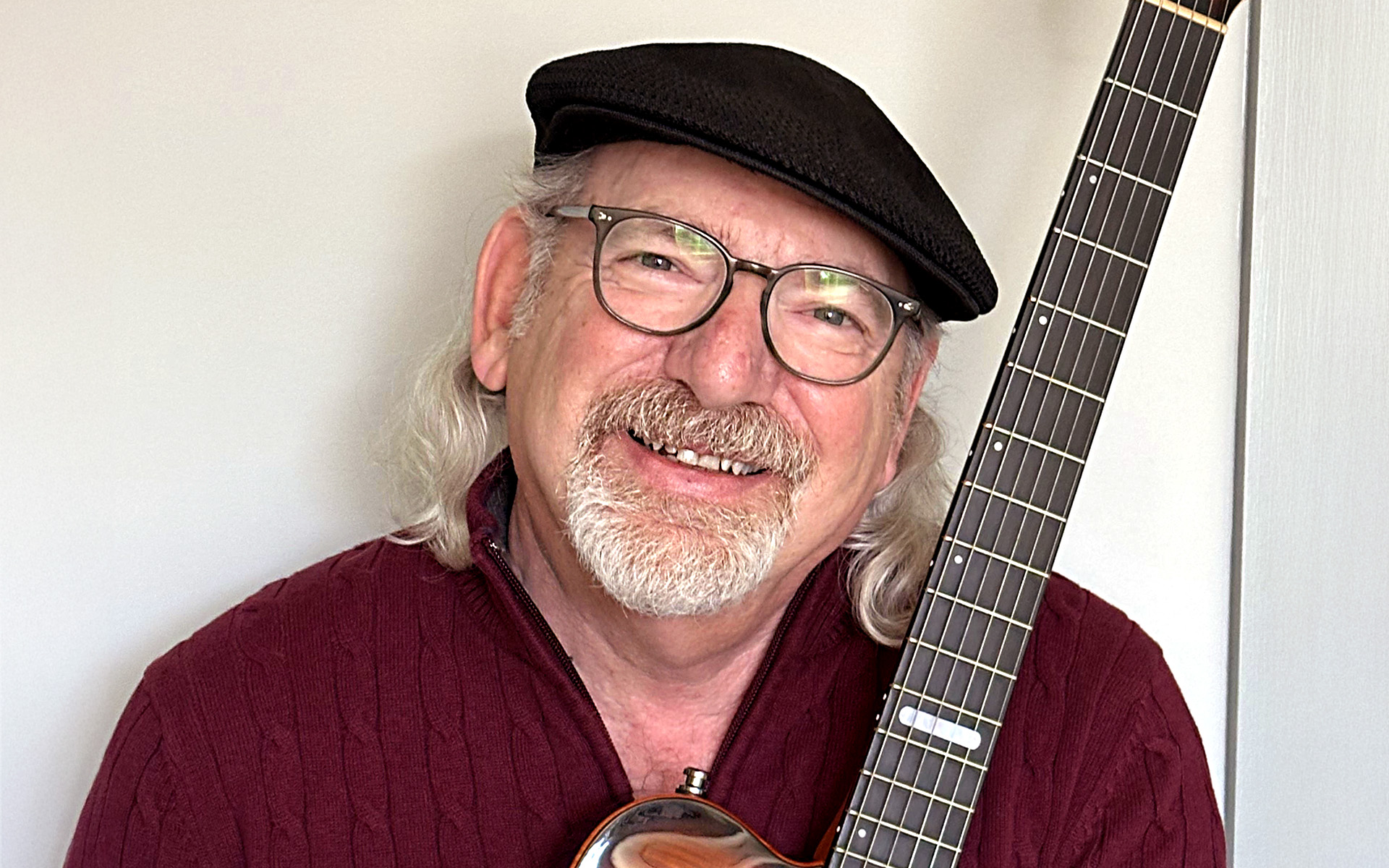David Mash, a Berklee Online course author and the former senior vice president of innovation, strategy, and technology for Berklee College of Music, stands against a white background, embracing one of the guitars he used to record his new album, titled Back to My Roots.