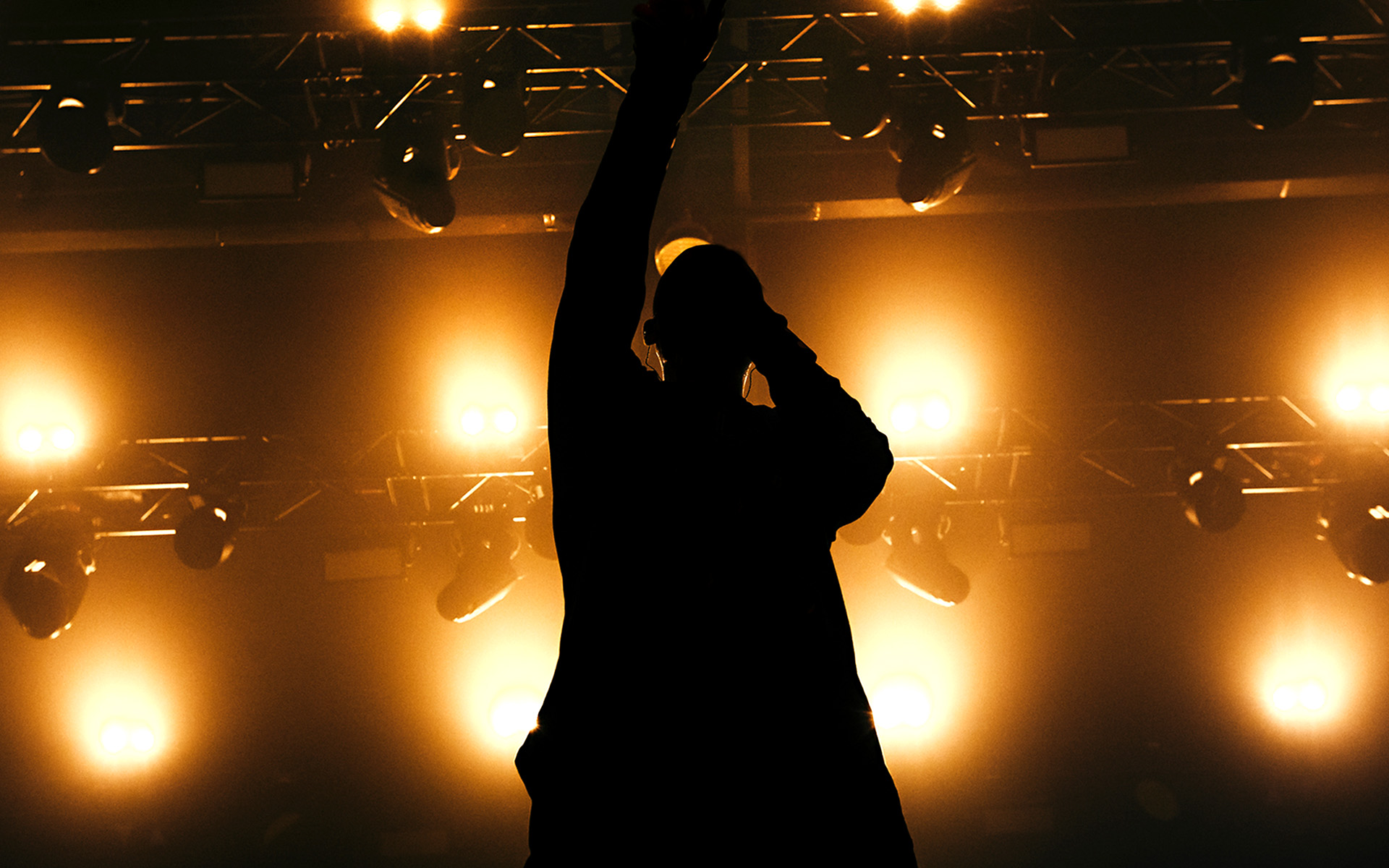 An MC raises a fist while rapping into a microphone during an onstage performance at a hip hop concert.