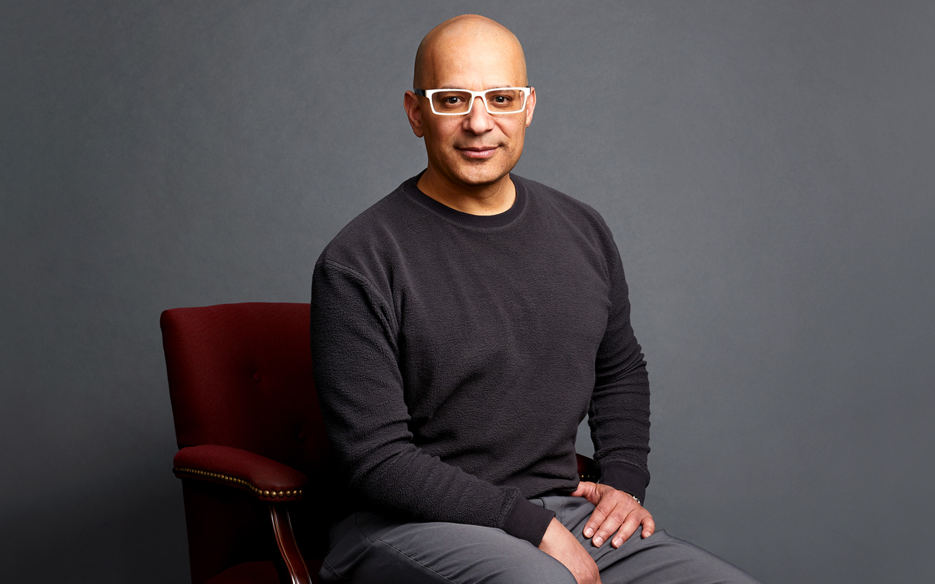 Rodney Alejandro sitting in a chair with a black shirt and gray background.