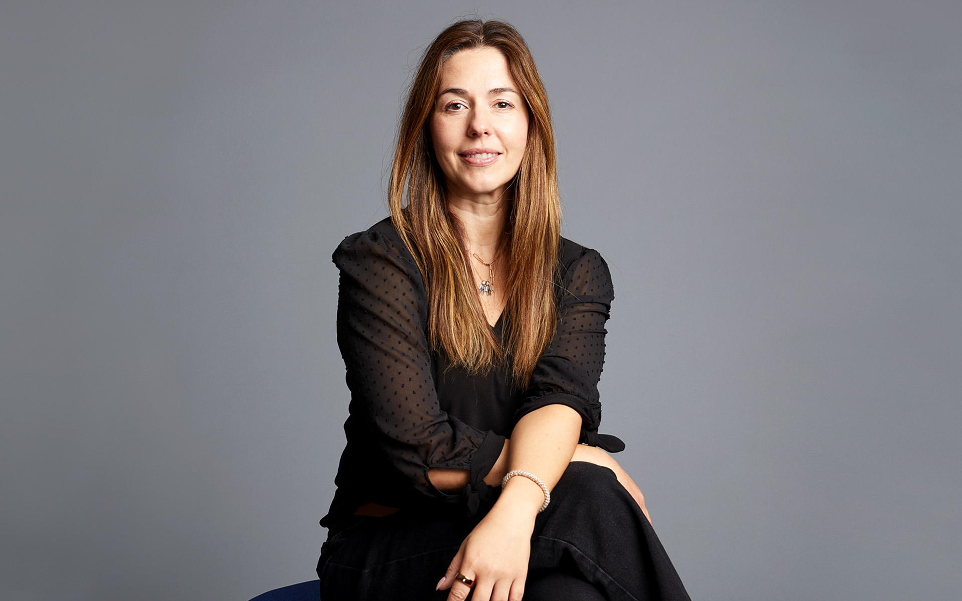 Vivian Aguiar-Buff sits cross-legged and looks directly at the camera in this portrait set against a gray background