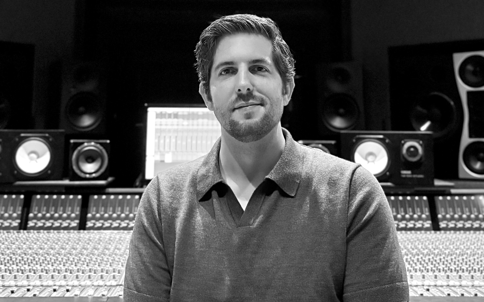 A black and white photo of Andrew Veres in front of a soundboard.