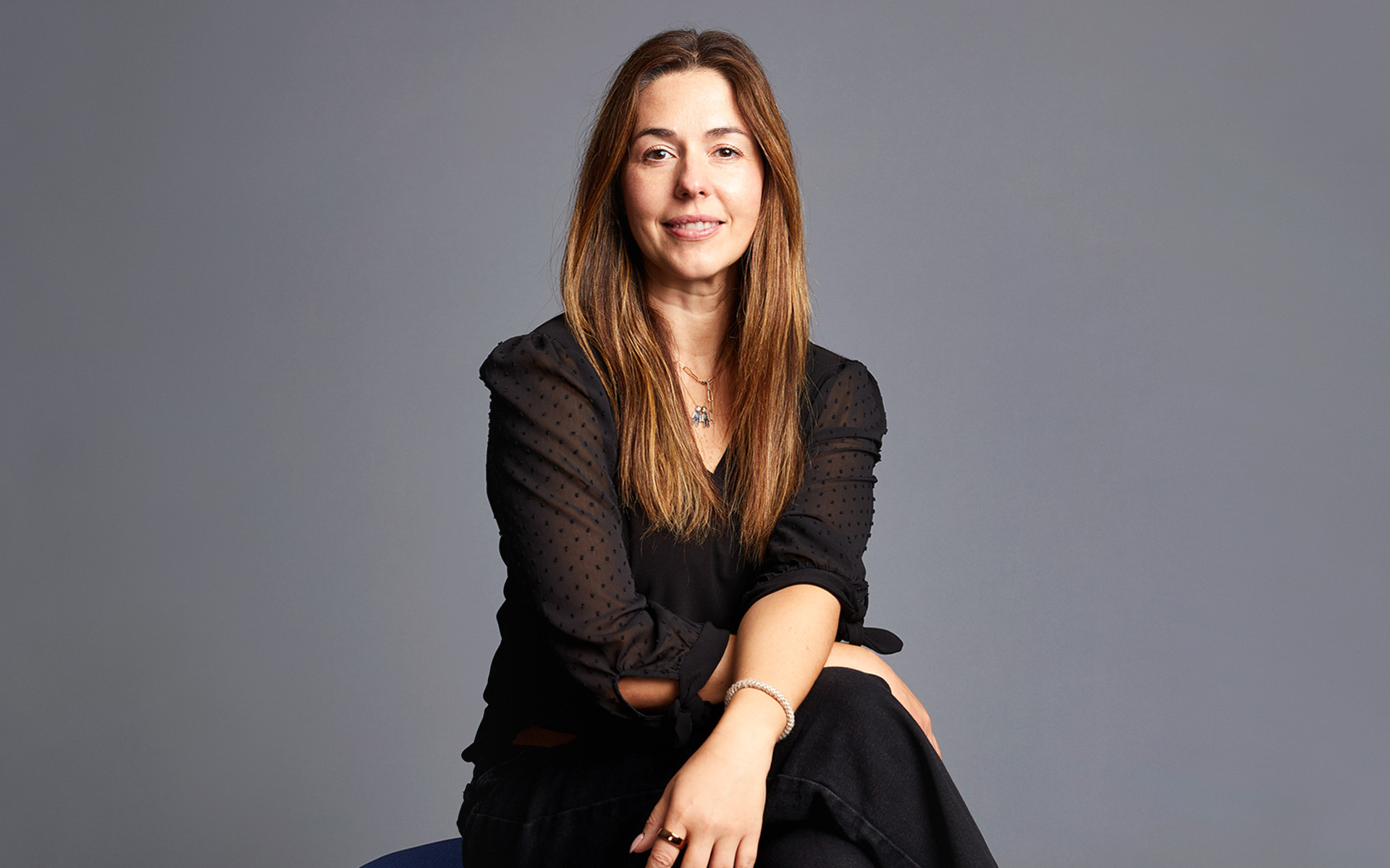 Vivian Aguiar-Buff sits cross-legged and looks directly at the camera in this portrait set against a gray background.