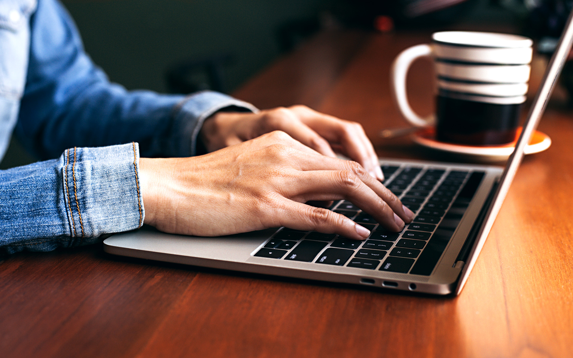 A person wearing a denim shirt sits at a computer, presumably typing out an application for a grant.