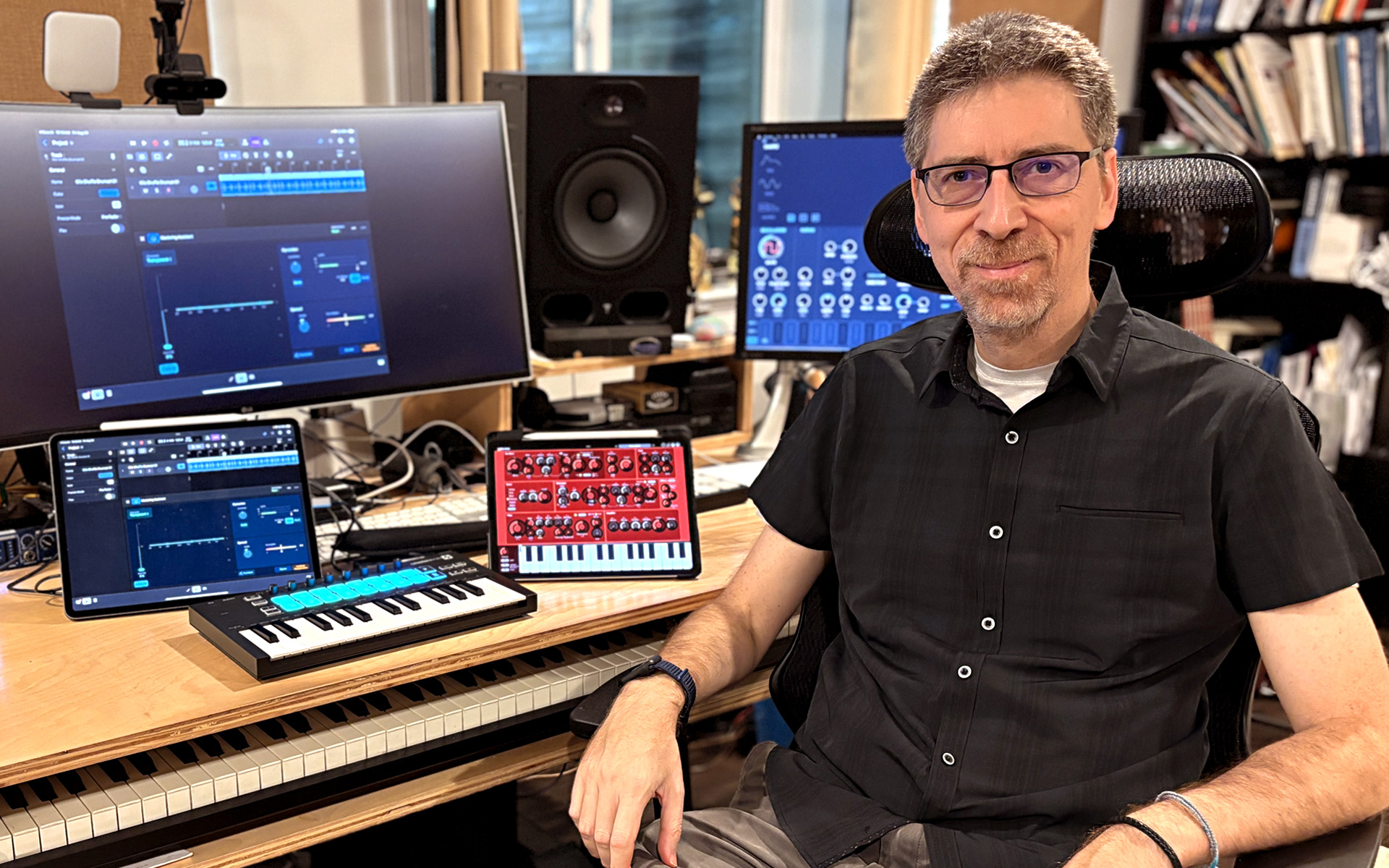 Andrea Pejrolo sits in front of a desk with various electronic devices and musical instruments, including two iPads, which are significant to him because he teaches the Music Writing and Production with the iPad course at Berklee Online.