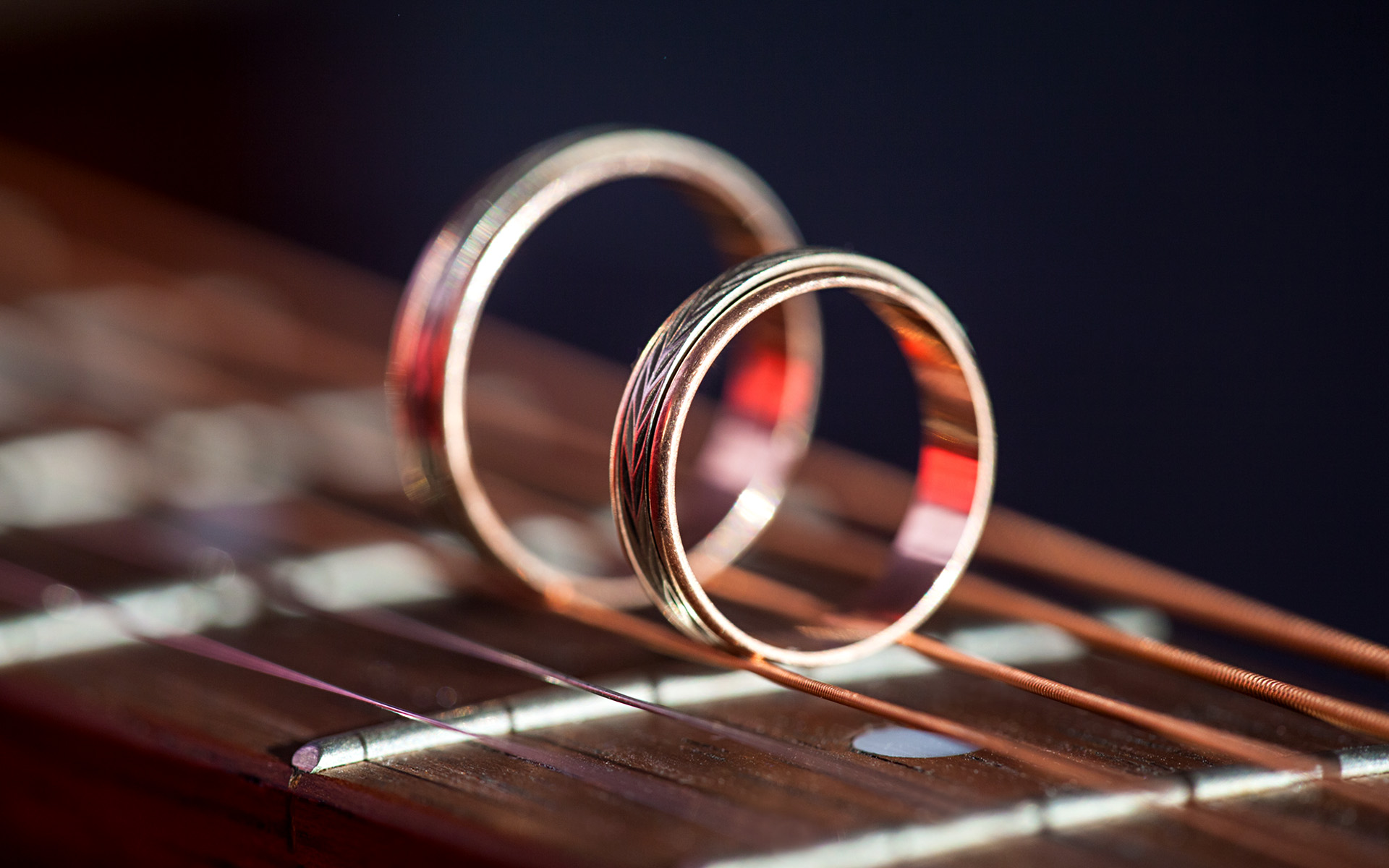 A pair of wedding rings sit on the fretboard of an acoustic guitar.