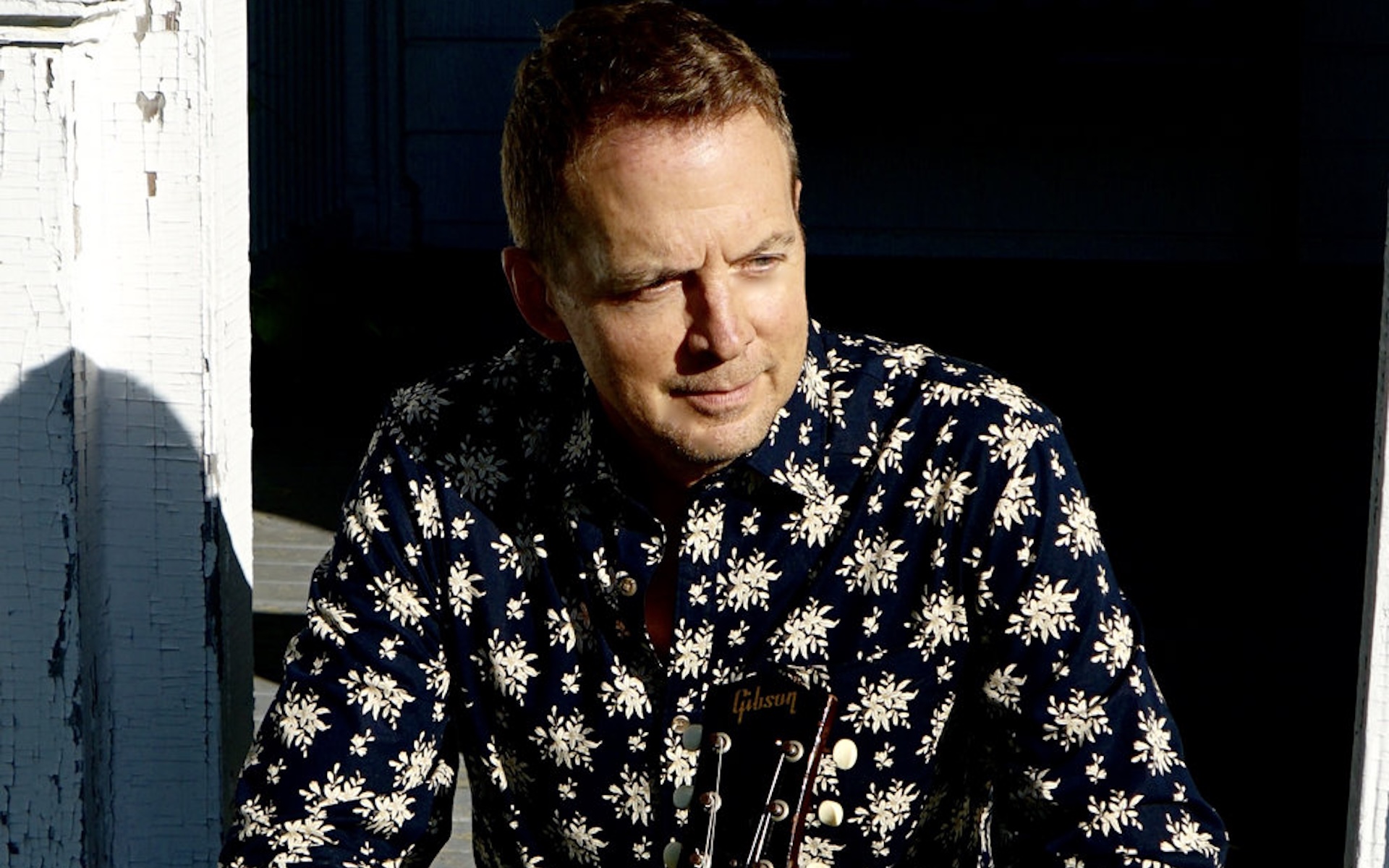 Photo of guitarist Julien Kasper, sitting in the sunshine with his guitar.