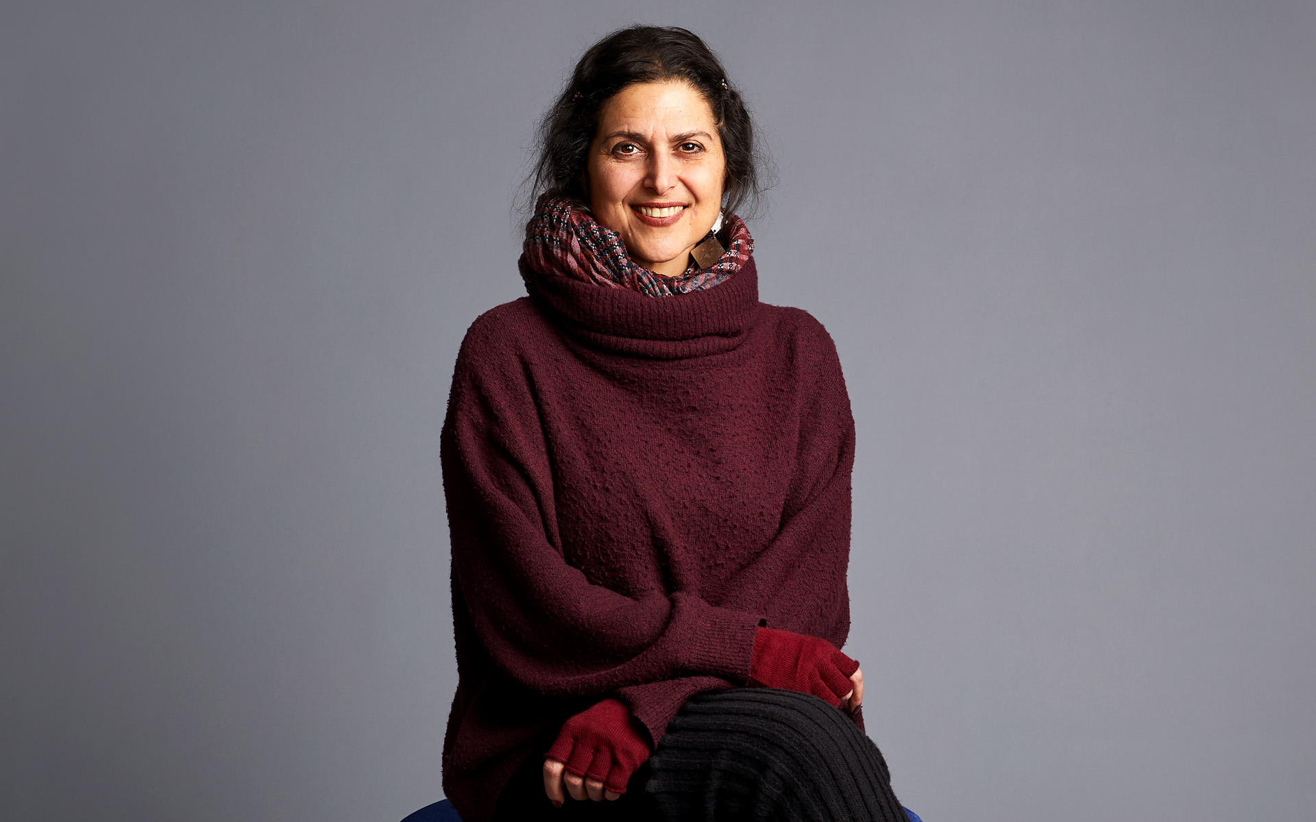 Christiane Karam sits cross-legged and looks directly at the camera in this portrait set against a gray background.
