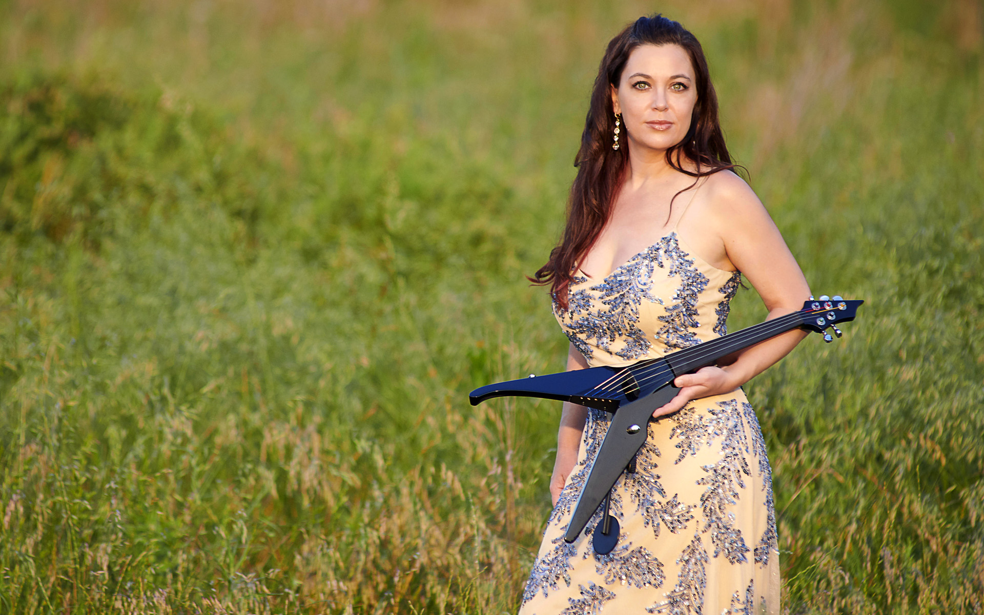 Jocelyn Rowland Khalaf stands in a green field, wearing a formal gown and holding a violin in the classic heavy metal shape of a flying V. Photo courtesy of Nathan Harmony Photography.