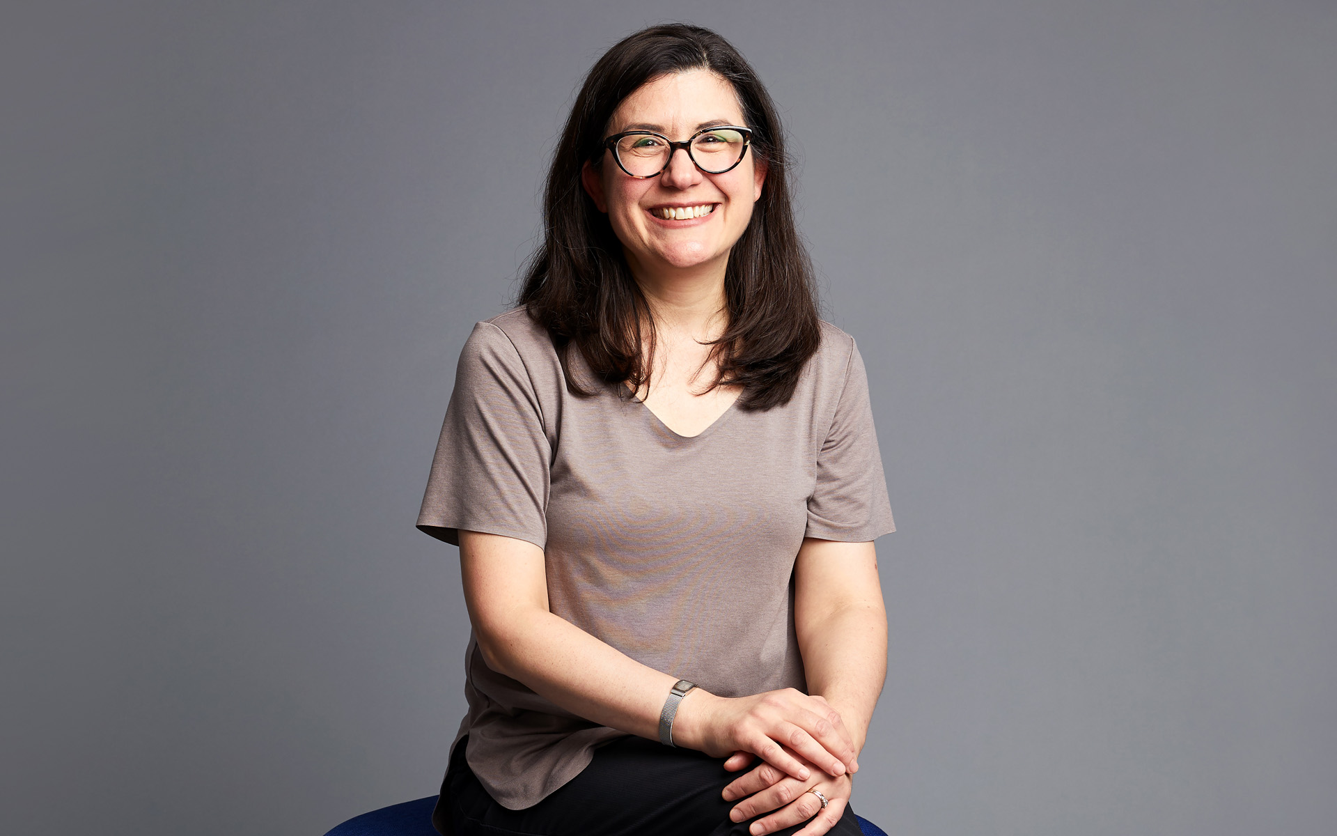 Amanda Monaco sits cross-legged and looks directly at the camera in this portrait set against a gray background.