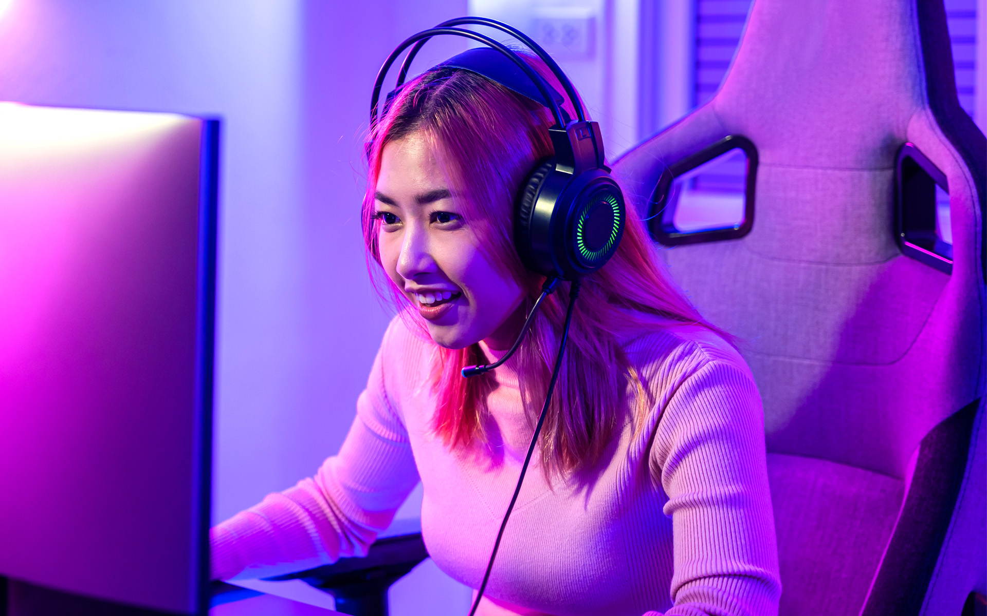 A woman sits at her computer with headphones on, presumably making adjustments to the sound design she has made for a video game.